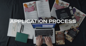 An overhead shot of application documents, university brochures, and a laptop displaying UCAS website, representing the application process complexity.