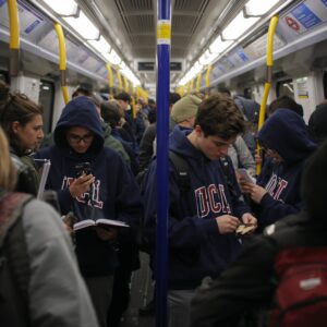 UCL university students studying lecture notes while commuting on crowded London Underground Northern Line during morning rush hour, depicting urban campus experience